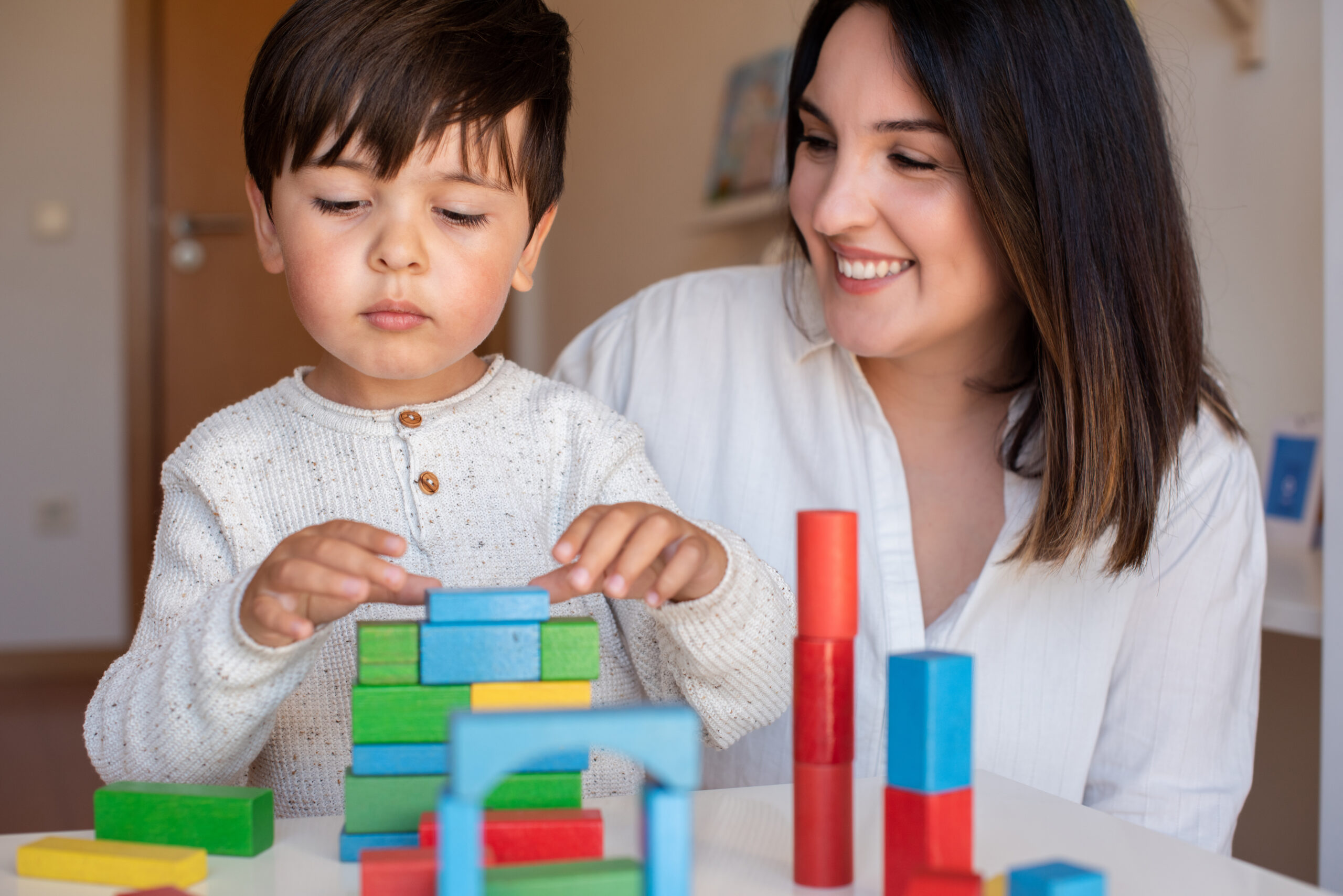 liltle preschooler kid playing with wood blocks teacher educador help homeshooling learning community montessori school scaled